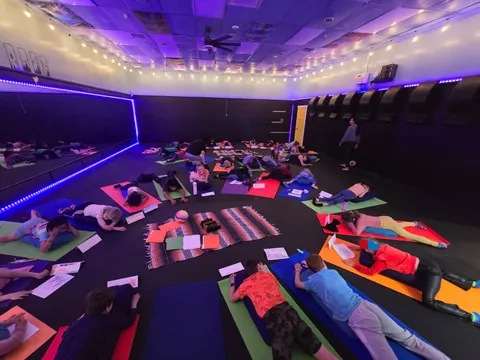 Students resting on their mats under purple studio lights
