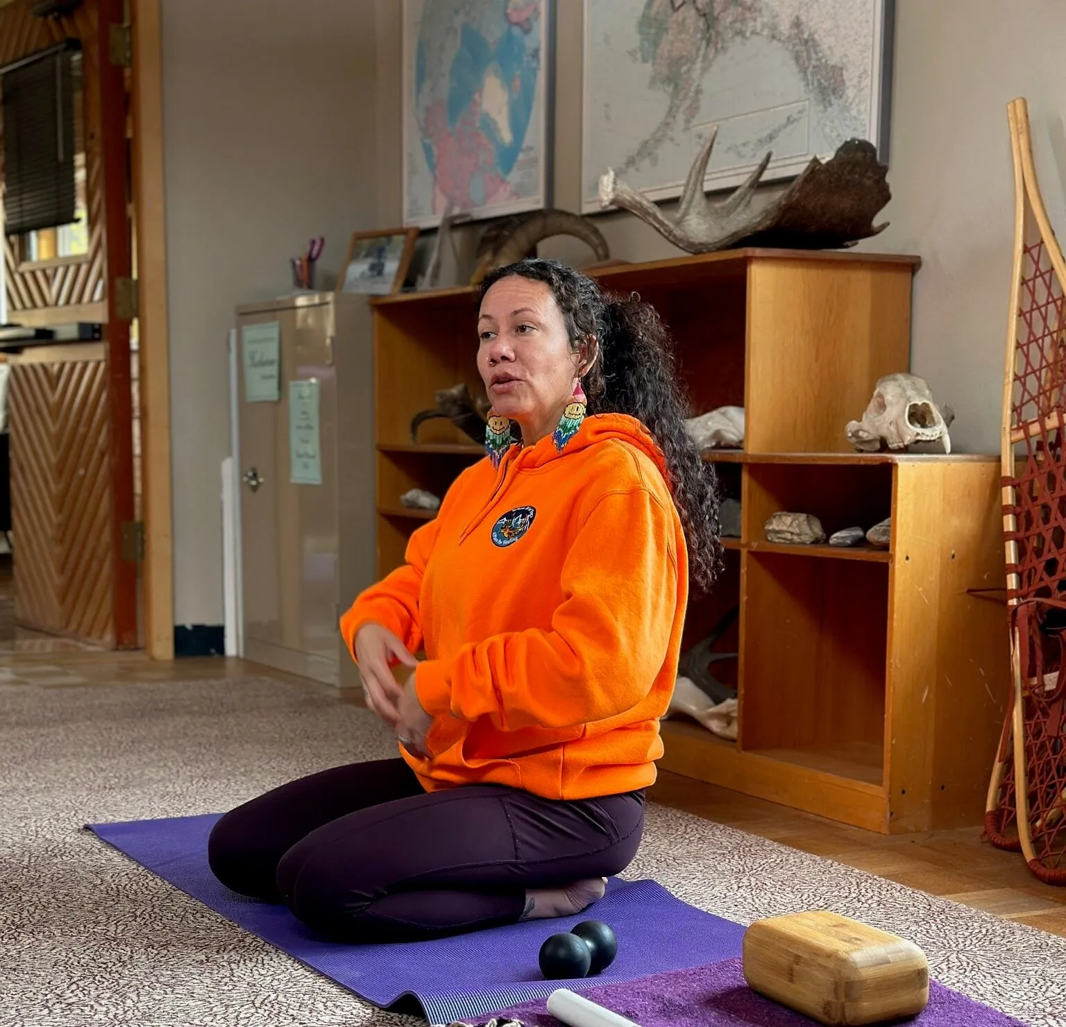 An instructor in an orange hoodie teaching from her mat