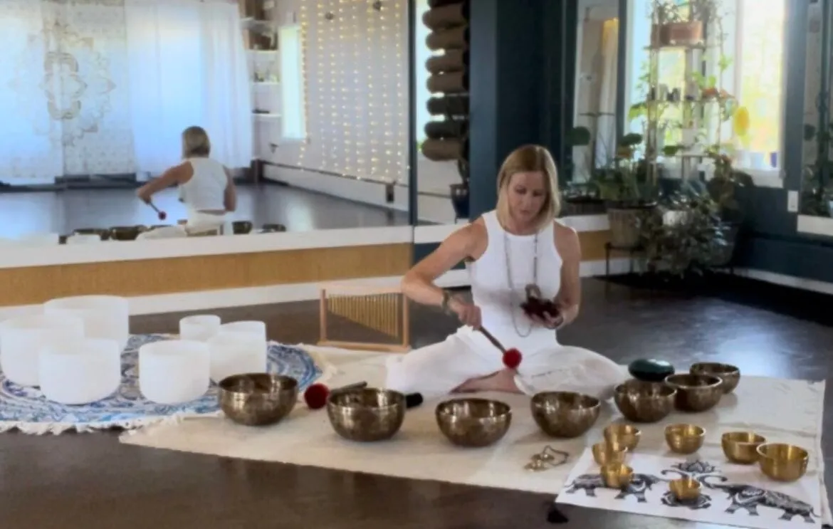 Practitioner playing crystal and brass singing bowls laid out on the studio floor